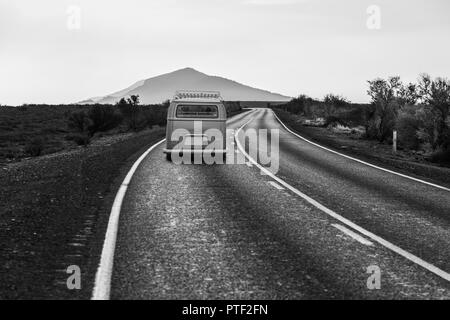 Minivan vecchia guida su strada tortuosa che conduce a una montagna panoramica picco in bianco e nero Foto Stock