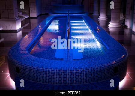 Un lusso pillared spa hall con gli illuminati piscina a tuffo nel centro. Un vuoto che la bella blu-piastrellate piscina spa dell'hotel deluxe. Colonne di parete sa Foto Stock