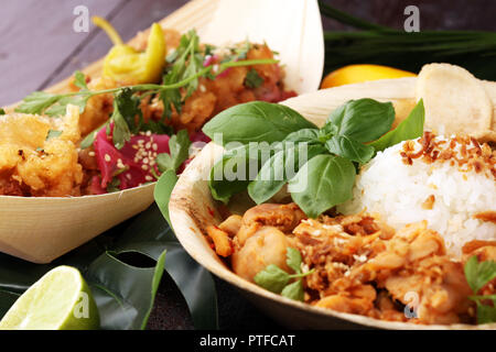Vari cibi da strada con ali di pollo su sfondo rustico Balinese. nasi campur e indiana e brasiliana cibo di strada Foto Stock