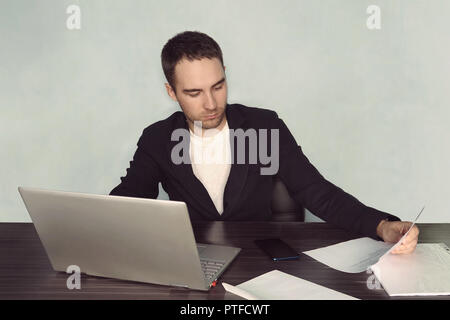 Immagine unshaved concentrato imprenditore 30s in t-shirt bianca con detenzione e guardando negli appunti con documenti cartacei durante il lavoro in ufficio. stanco lavoratore Foto Stock
