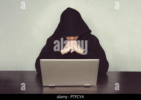 Hacker con il suo computer pensando su fondo azzurro. monaco eremita orante nella parte anteriore del computer. concetto di criminalità informatica e hacking electroni Foto Stock