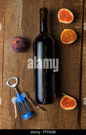 Appartamento vista laici della bottiglia di vino rosso con frutti di fichi e melograno, sul vecchio brown tavolo in legno, verticale. Foto Stock