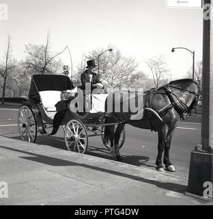 Anni sessanta, storico open-top cavallo e carrozza con autista in abito formale e top hat, in attesa di clienti da parte di central Park di New York, New York, Stati Uniti d'America. Foto Stock