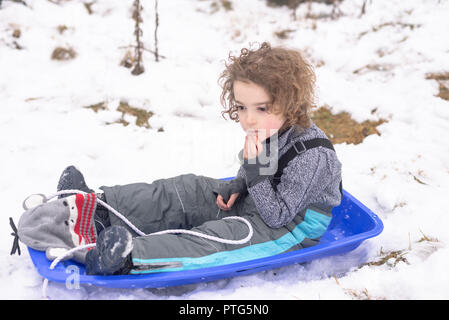 Ritratto di un ragazzo seduto in una pista da slittino in attesa di andare in slittino Foto Stock