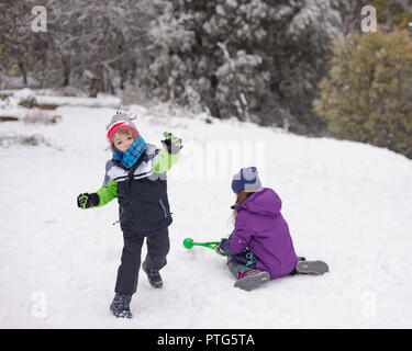 Giovane ragazzo lancia una palla di neve mentre una giovane ragazza rende più snowballs Foto Stock