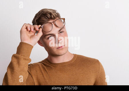 Un fiducioso giovane in un studio, tenendo gli occhiali sulla sua fronte. Foto Stock