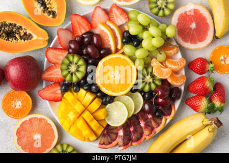 Materie frutti bacche platter, mango, arance e kiwi fragole, mirtilli pompelmo uva, banane mele sulla piastra bianca, sul bianco tabl Foto Stock