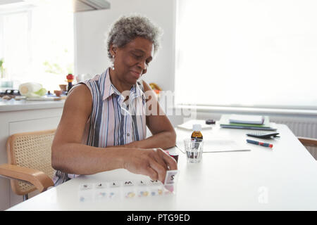 Senior donna organizzando pillola box al tavolo della cucina Foto Stock