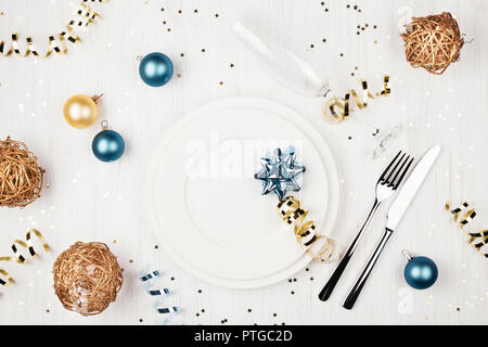 Tavola di natale con impostazione blu e palline dorate, serpentine e bagliori di colore bianco su un tavolo di legno. Overhead. Foto Stock