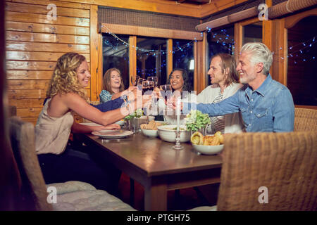 Gli amici di tostatura vino rosso bicchieri, di gustare la cena in cabina tavolo da pranzo Foto Stock