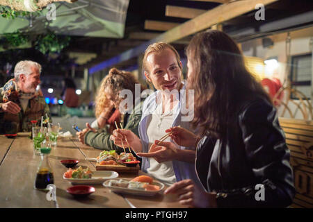 Paio mangiare godendo di sushi sul patio di notte Foto Stock