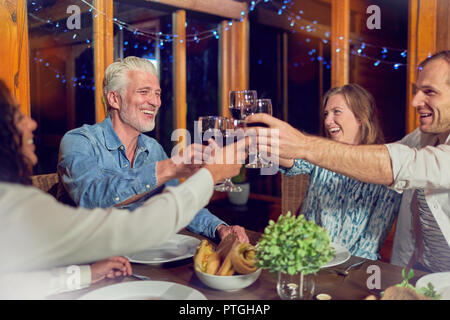 Amici celebrando, bere vino rosso e di gustare la cena in cabina Foto Stock