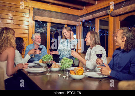 Amici celebrando, bere vino rosso e di gustare la cena in cabina Foto Stock