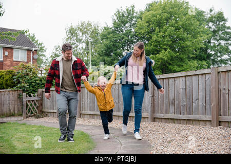 Ragazzino che tiene i suoi genitori le mani come essi a piedi lungo il sentiero per tornare a casa. Essi sono a sorridere e ridere sulla via del ritorno. Foto Stock