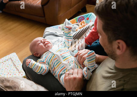 Mid-adulto padre giocando e tenendo la sua new born baby boys gambe e cercando di comfort di lui mentre è il pianto. Foto Stock