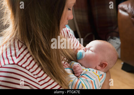 Close-up di una madre seduta sul divano di casa e tenendo premuto il suo neonato Bambino addormentato tra le sue braccia. Foto Stock