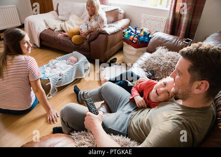 Tre generazioni di una famiglia sono rilassanti, guardando la tv e parlando nel soggiorno di casa propria. Foto Stock