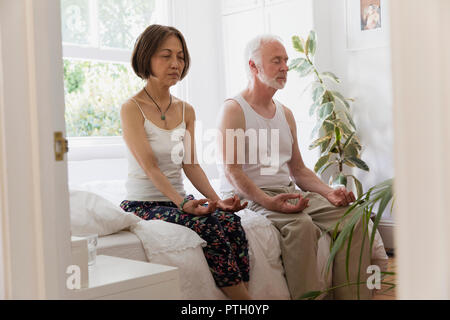 Serena coppia senior meditando sul letto Foto Stock