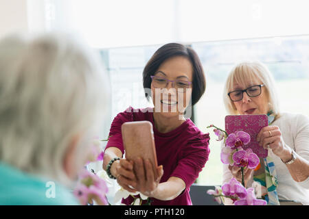 Attiva le donne anziane con la fotocamera del telefono a fotografare le orchidee in fiore disponendo di classe Foto Stock