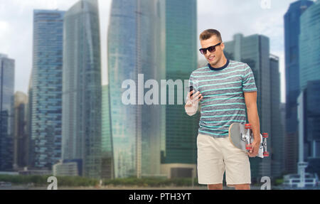 Uomo con lo skateboard e lo smartphone su Singapore Foto Stock