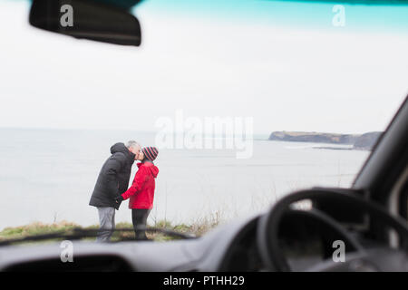 Coppia affettuoso bacio al di fuori di casa a motore sulla scogliera con vista sull'oceano Foto Stock