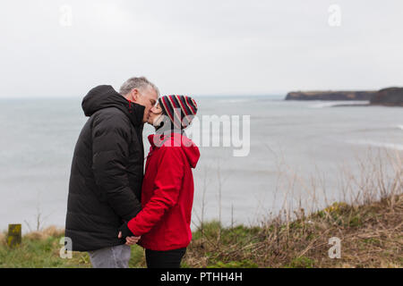 Coppia affettuoso bacio sulla scogliera con vista sull'oceano Foto Stock