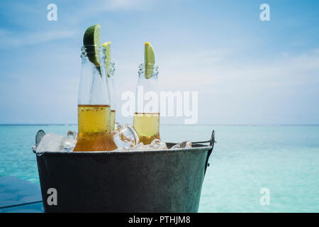 Fettine di lime in bottiglie di birra sul ghiaccio sulla tranquilla spiaggia dell'oceano, Maldive, Oceano Indiano Foto Stock