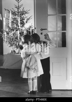 Natale nel 1940s. Due ben vestito i bambini sono in piedi la porta di ingresso alla camera dove l'albero di Natale e regali di Natale. La ragazza ha un bel vestito di bianco e il ragazzo un tipico ragazzo sailor suit. La Svezia 1940s Foto Stock