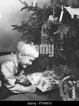 Natale nel 1940s. Un giovane ragazzo è curioso di vedere qual è il regalo di Natale che giace sotto un albero di natale. La Svezia 1940s Foto Stock