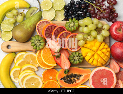 Sani frutti colorati nei colori dell'arcobaleno, fragole, mango, uva, banane, pompelmo sul bianco tabella, vista laterale, il fuoco selettivo Foto Stock