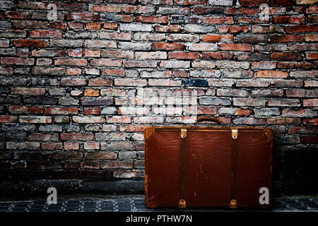 Vecchia valigia abbandonata vicino a un muro nel decadimento Foto Stock