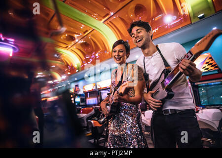 Giovane godendo di un gioco musicale di chitarra presso il gioco arcade. Coppia felice suonare la chitarra di gioco arcade giochi holding chitarre. Foto Stock