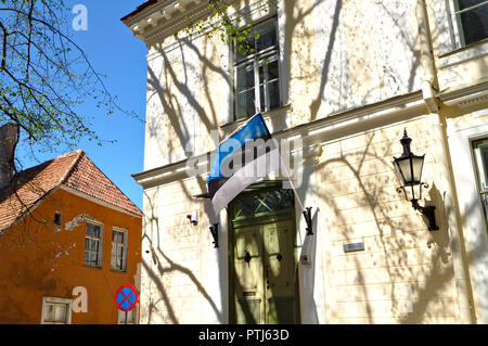 Bandiera estone sul muro di un edificio nella città vecchia di Tallinn. Muro beige di un vecchio edificio coperto con le ombre di alberi. Bandiera appeso accanto a t Foto Stock