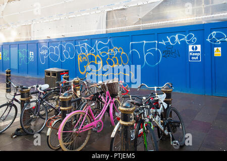 Biciclette concatenati per Rastrelliere per biciclette su un marciapiede davanti al sito in costruzione cartelloni coperto di graffiti tag nel centro di Cardiff in Galles. Foto Stock