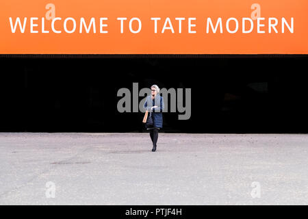 Una donna matura a piedi nella parte anteriore di un segno di benvenuto al di sopra di un ingresso alla Tate Modern sulla South Bank di Londra. Foto Stock