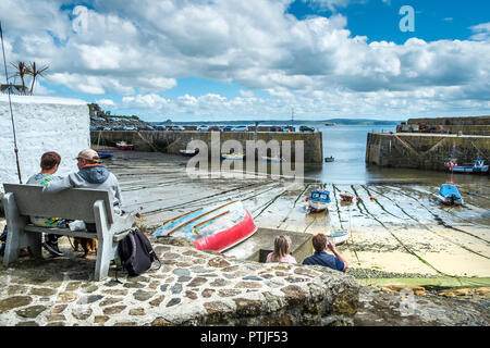 Vacanzieri relax sui posti a sedere con vista porto Mousehole in Cornovaglia. Foto Stock