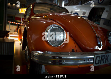 Arty a basso angolo, paesaggio close up di bruciato di colore arancio Volkswagen maggiolino, dalla parte anteriore. Vettura è ferma all'interno di exhibition hall. Foto Stock