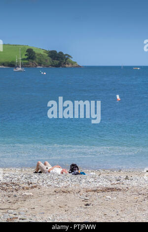 Un uomo a prendere il sole sulla spiaggia privata a Polgwidden Cove lungo il fiume Helford vicino al passaggio di Helford in Cornovaglia. Foto Stock