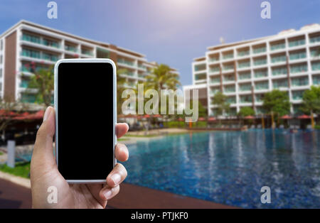 Mano d'uomo mostra mobile smartphone in posizione verticale mock up del modello e sfocato hotel sfondo per il tuo libro bussiness hotel. Foto Stock