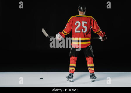 Vista posteriore del giocatore professionale del hockey di ghiaccio azienda mazza da hockey su nero Foto Stock