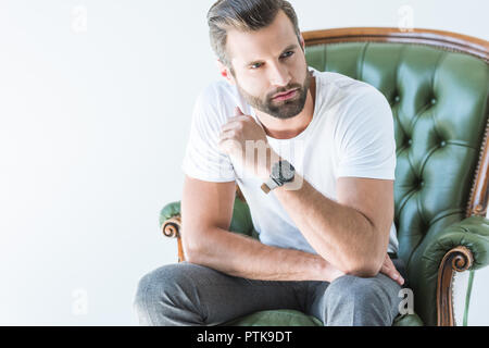 Brunet bel uomo seduto in poltrona verde, isolato su bianco Foto Stock