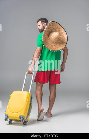 Vista posteriore del turista maschio in sombrero messicano a piedi con borsa da viaggio su grigio Foto Stock