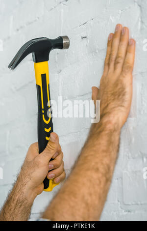 Immagine ritagliata della martellatura repairman chiodo conficcato nel muro bianco Foto Stock