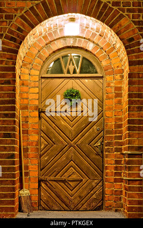 Ingresso illuminato con il vecchio decorata porta di legno. Testa tonda e piccola finestra sopra la porta. Circondata da mura di pietra. Foto Stock