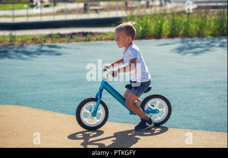 Un piccolo ragazzo gode di un equilibrio in bici su un parco giochi in un parco su un estate giornata di sole. Foto Stock