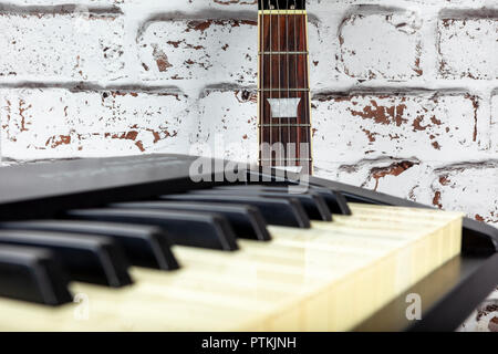 Chitarra elettrica appoggiata contro un bianco invecchiato parete dipinta dietro una tastiera di pianoforte Foto Stock