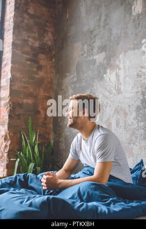 Sorridente giovane uomo svegliarsi nel suo letto durante la mattina tempo a casa Foto Stock