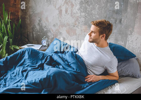 Fiducioso giovane uomo svegliarsi nel suo letto durante la mattina tempo a casa Foto Stock