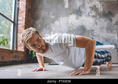 Fiducioso giovane uomo facendo spingere ups durante la mattina tempo a casa Foto Stock