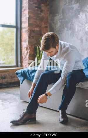 Giovane imprenditore lacci delle scarpe di legatura in camera da letto a casa Foto Stock